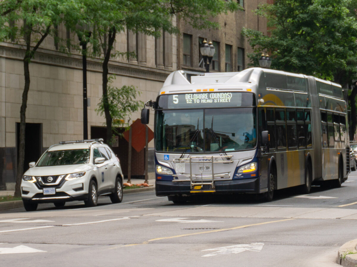 Photo shows a HSR supervisor car on the right, with a HSR 60-foot articulated bus to its left. Both are waiting at an intersection during a red light.