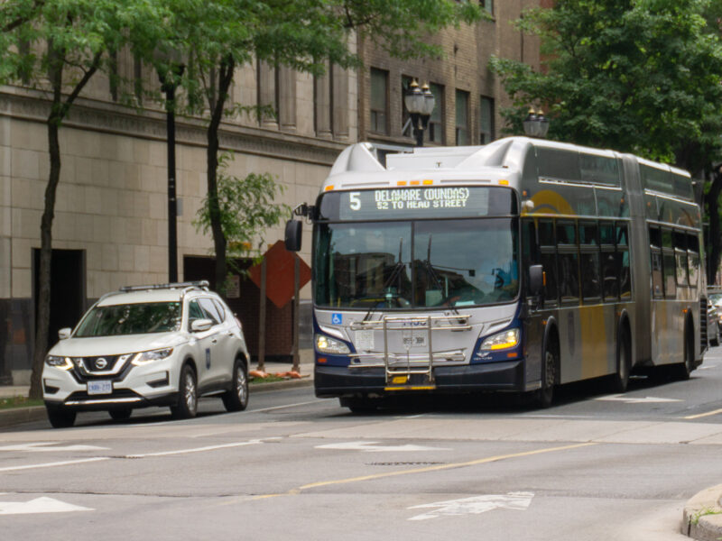 Photo shows a HSR supervisor car on the right, with a HSR 60-foot articulated bus to its left. Both are waiting at an intersection during a red light.