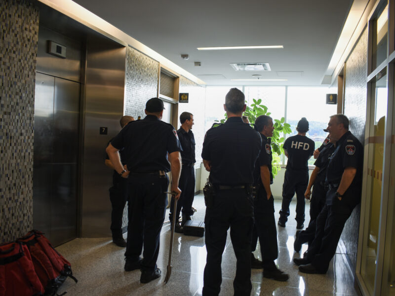 Hamilton firefighters standing in a lobby awaiting an elevator mechanic to rescue a person trapped inside a stalled elevator