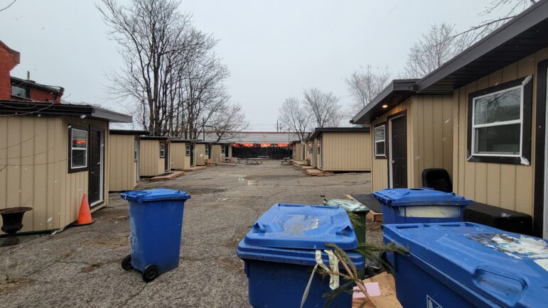 Wide-angle view of the 16-unit HATS tiny shelter community at 205 Cannon Street East in Hamilton, showing modular housing structures in March 2026.