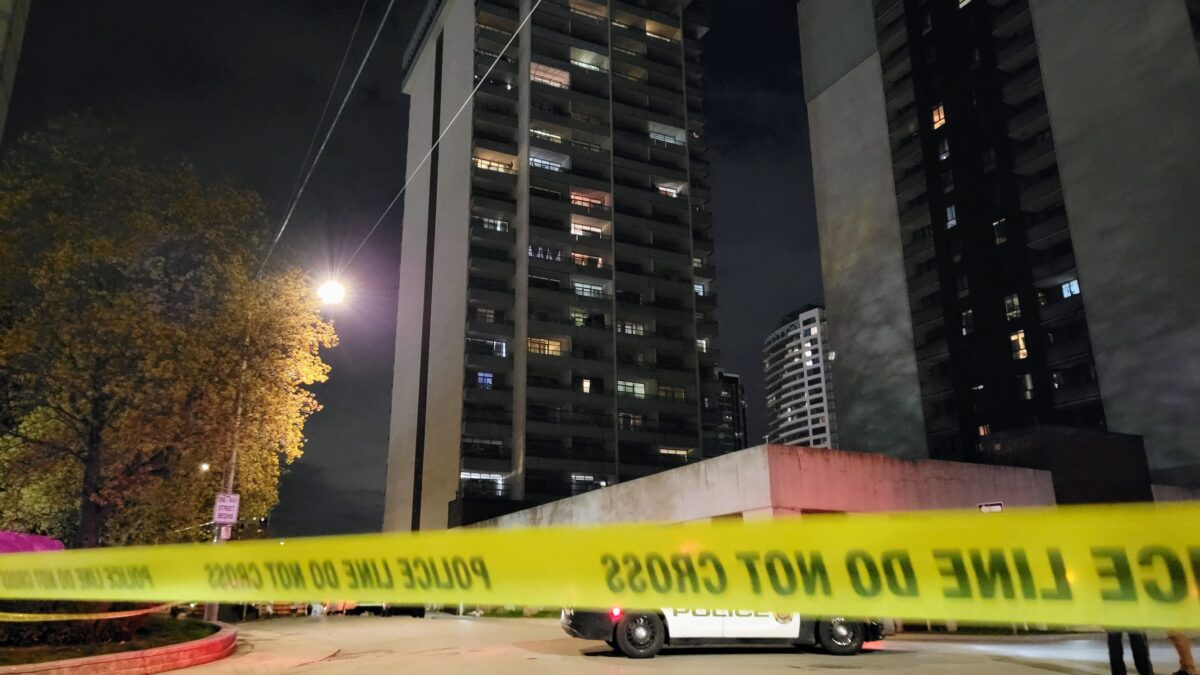 A nighttime view of a high-rise apartment building at 191 Main Street West. In the foreground, yellow "POLICE LINE DO NOT CROSS" tape is stretched across the frame, partially obscuring a parked police cruiser.